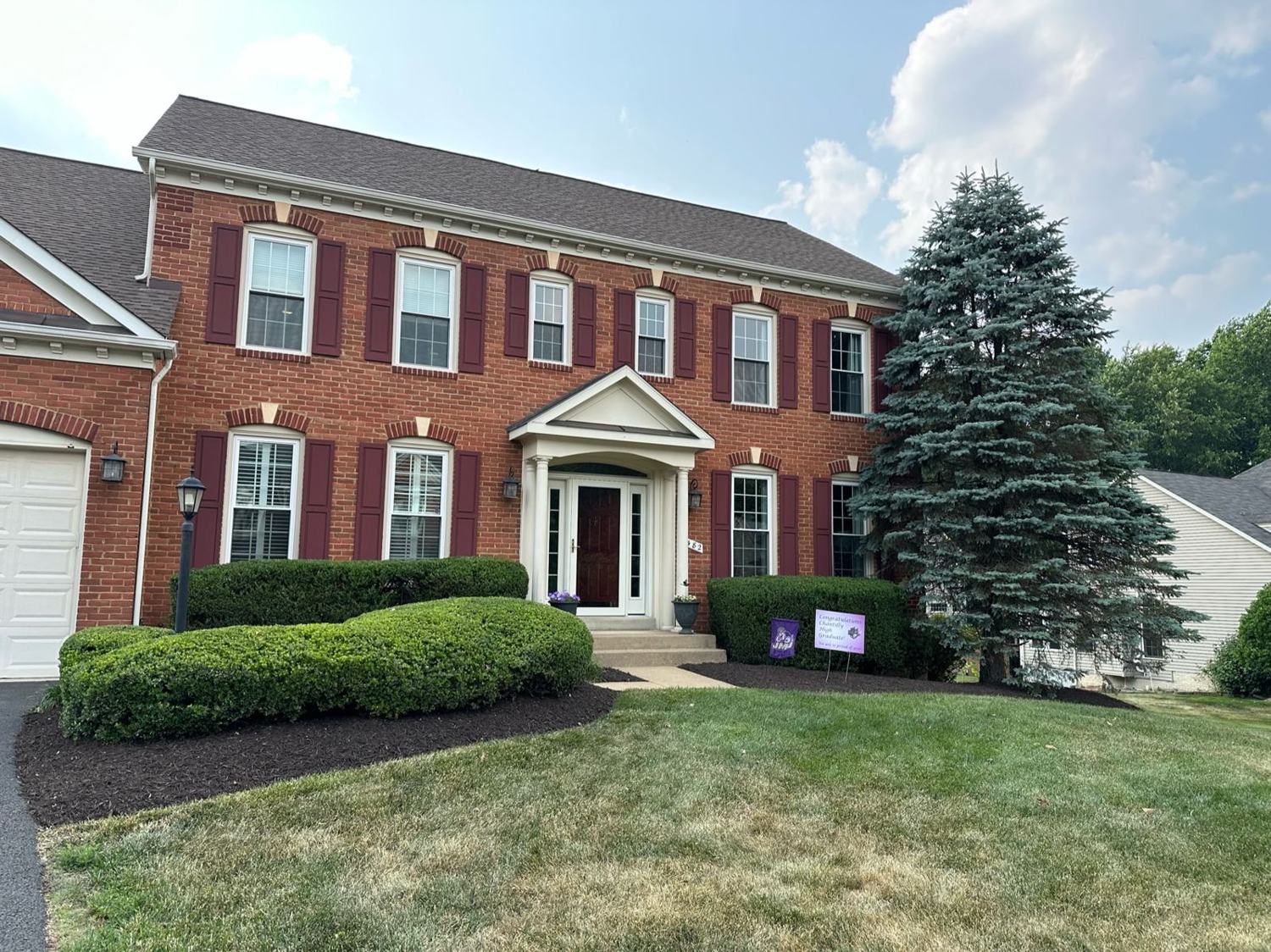 Brick colonial with a maintained lawn and foundation beds