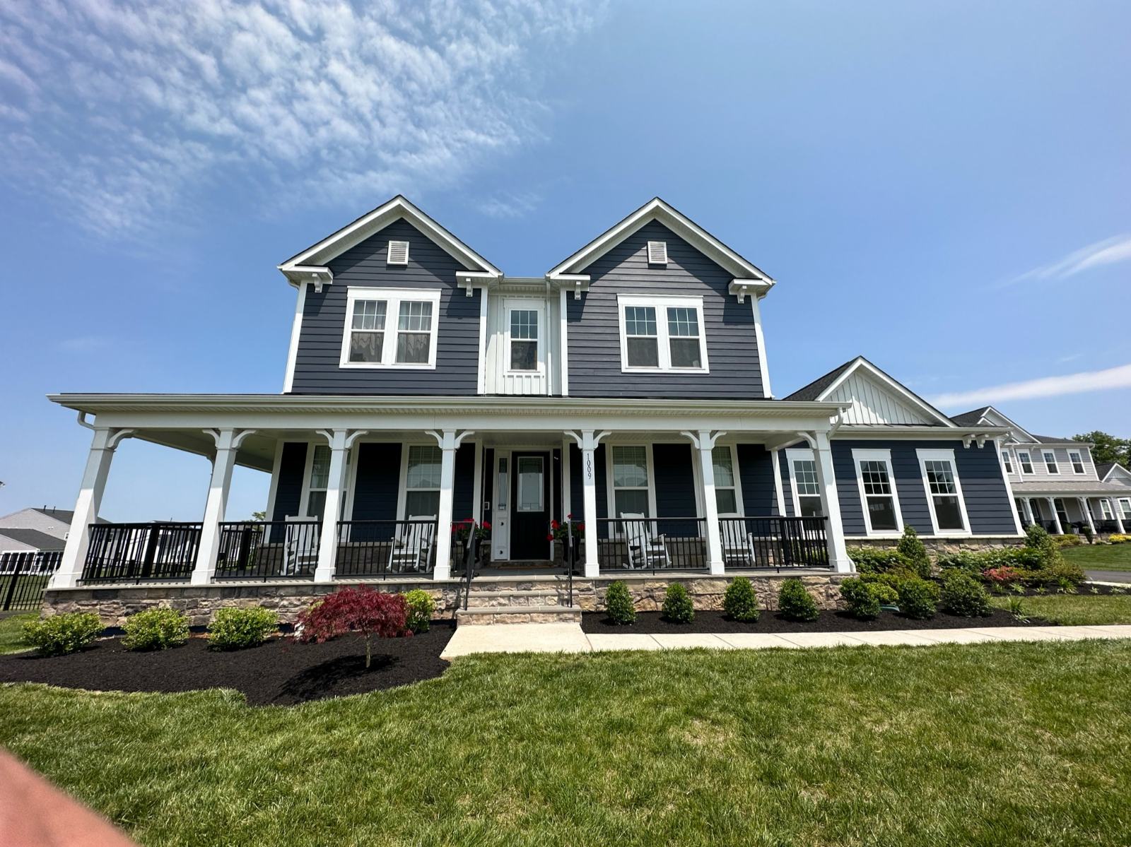 Full front landscape and foundation plantings on a navy farmhouse