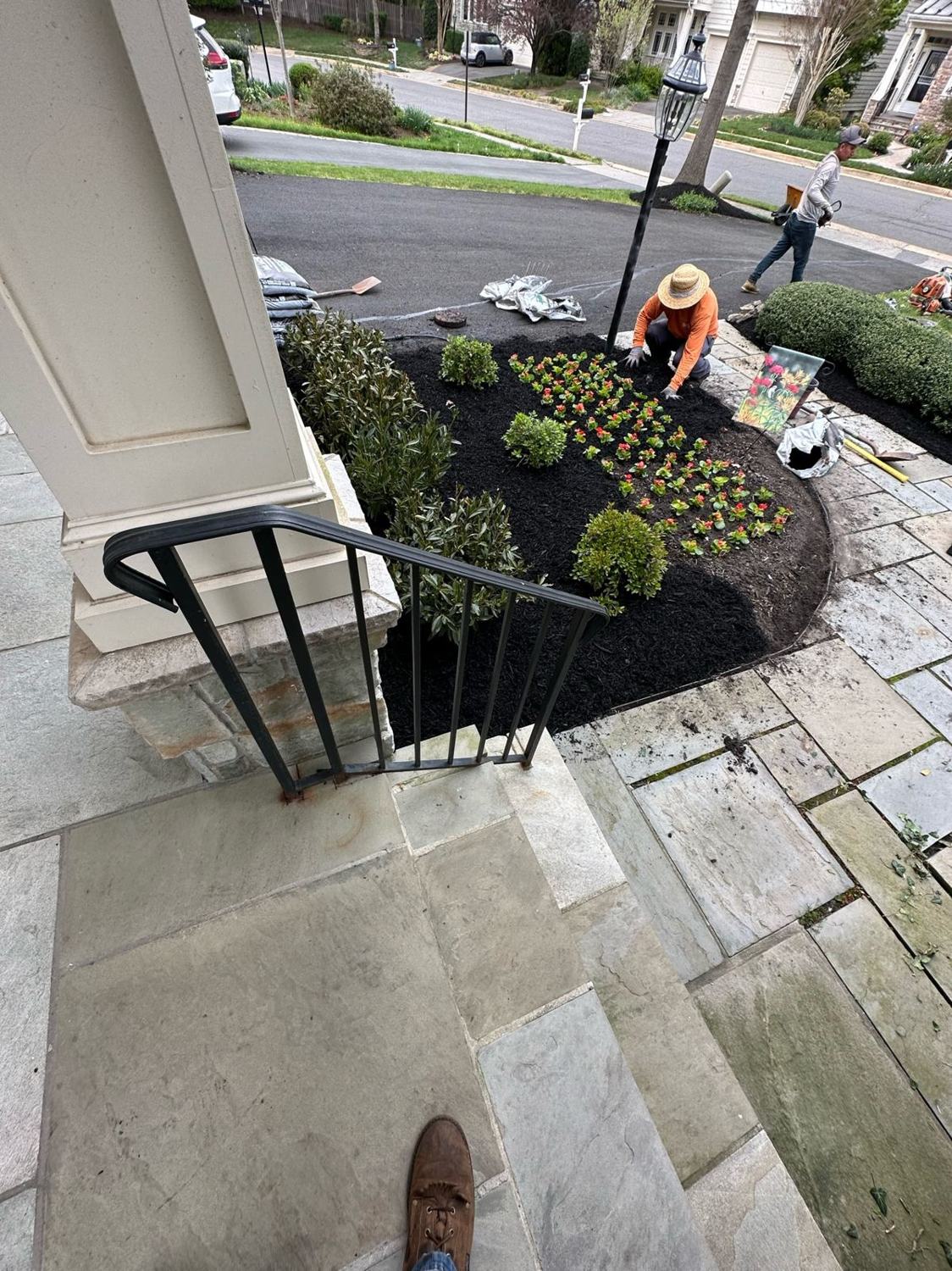 Crew member planting a mulched bed beside stone entry steps