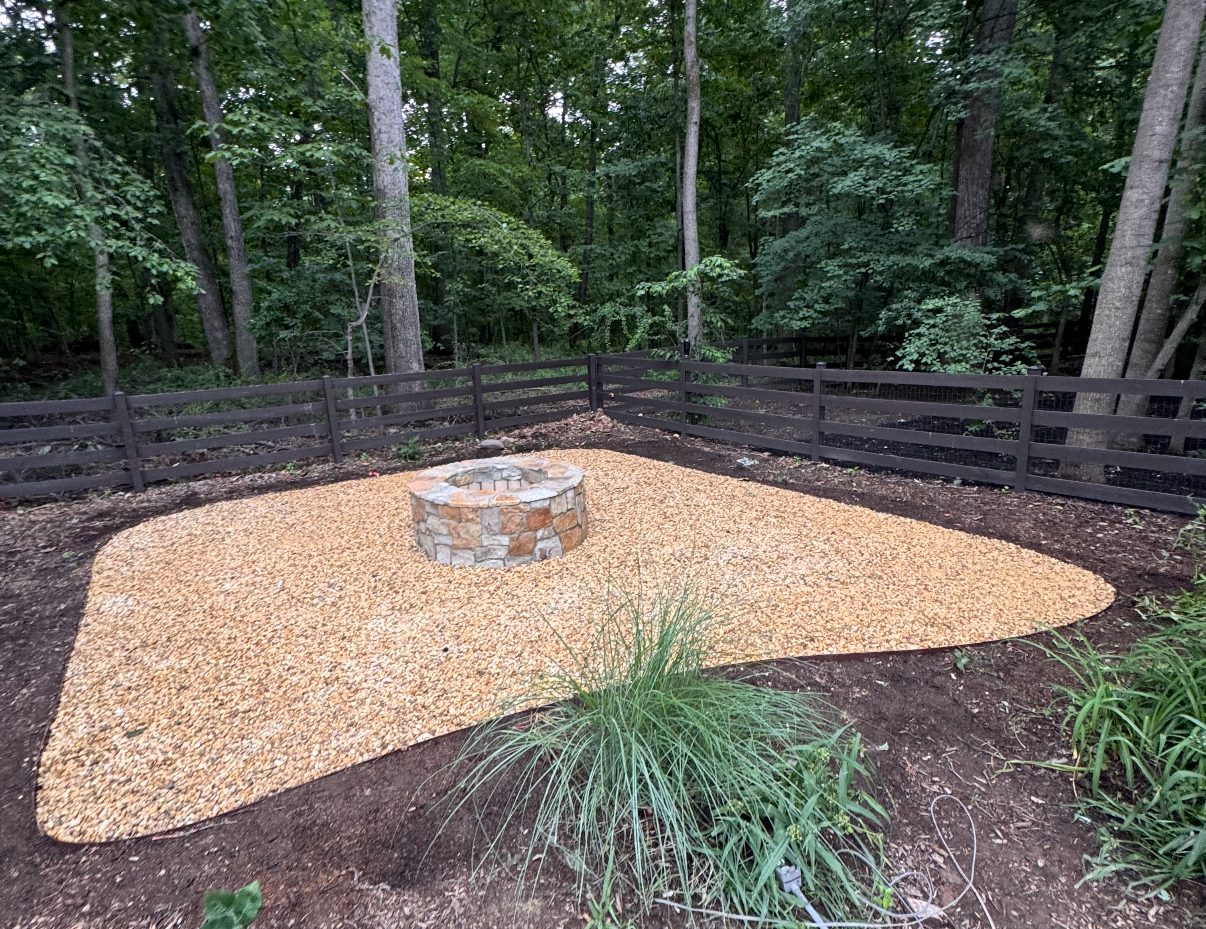 Stone fire pit on a river gravel seating area at the edge of the woods