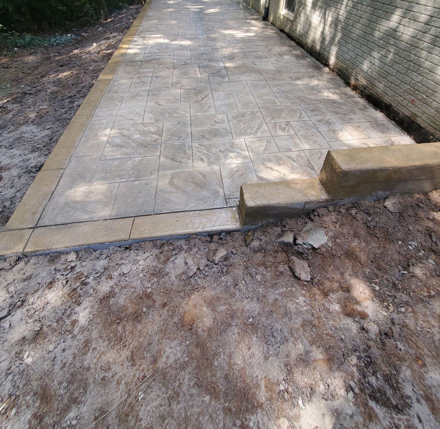 Long tan stamped concrete patio with a border along the back of a home