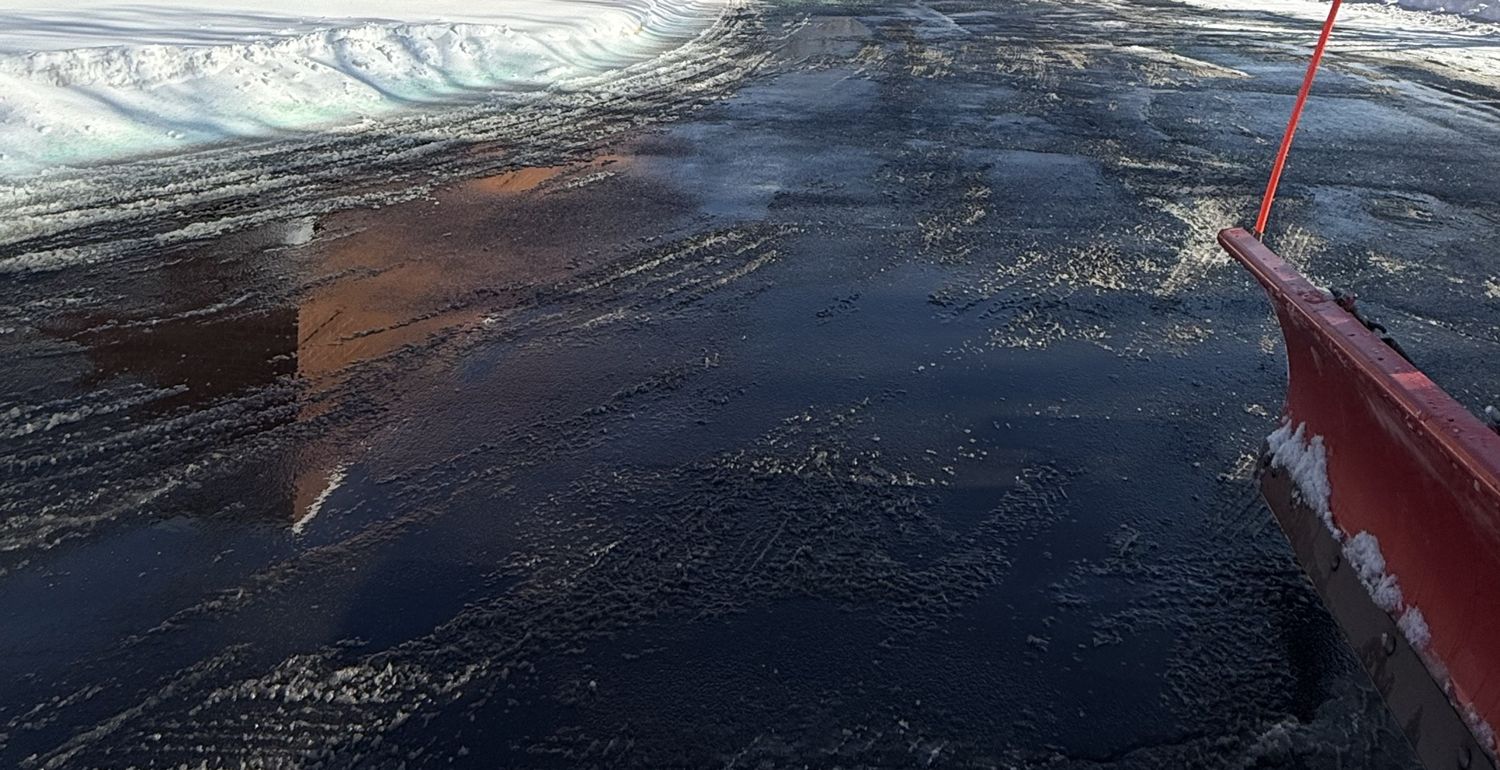 Commercial parking lot plowed down to wet pavement with snow banked at the edges