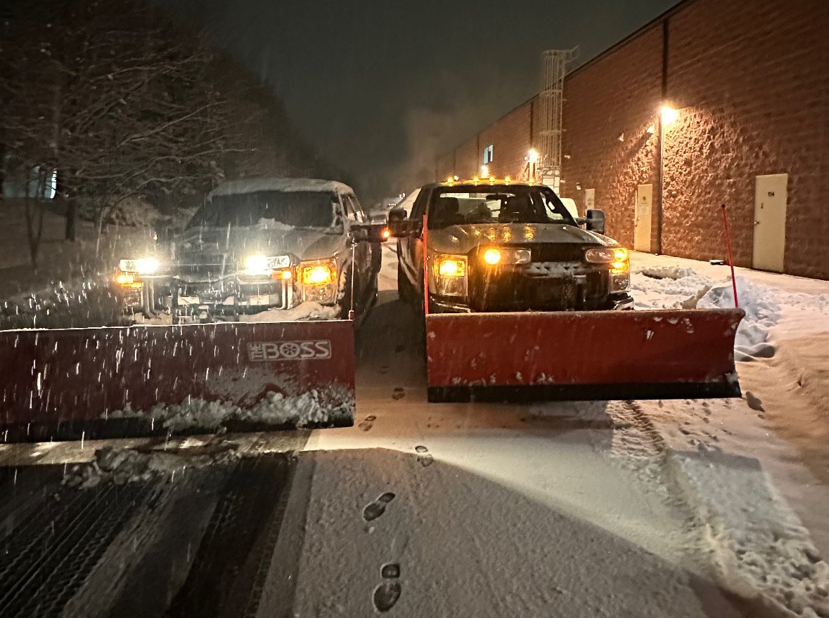 Two plow trucks clearing a service lane at night